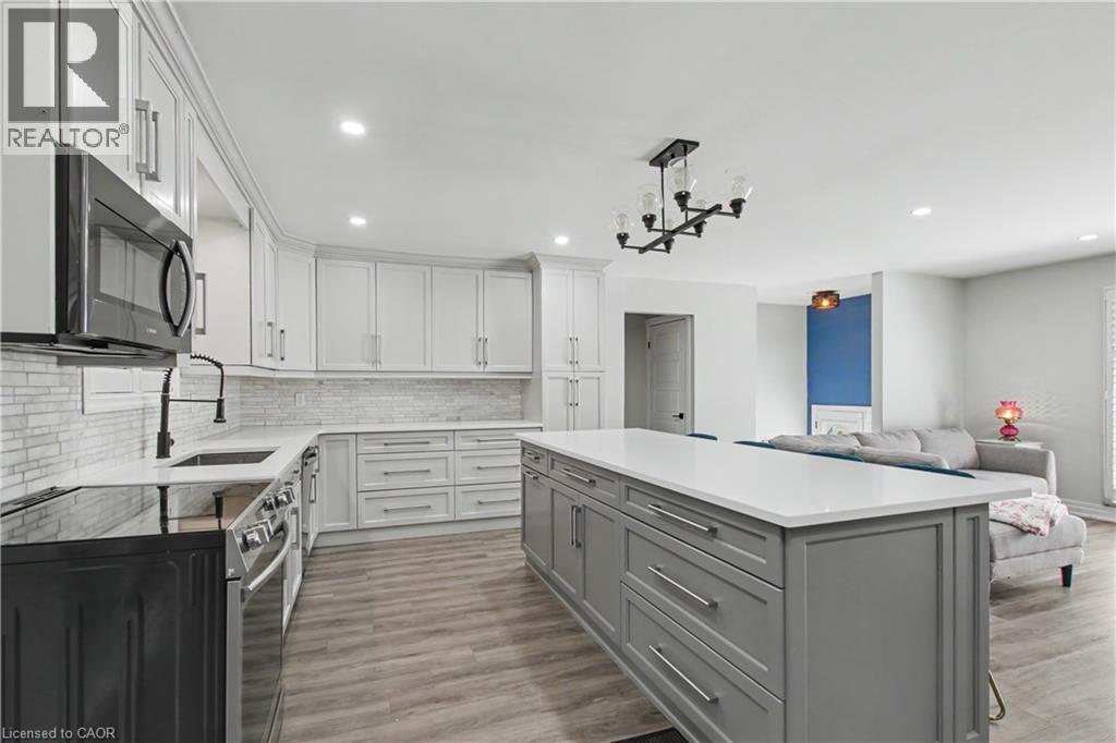 Modern kitchen featuring white shaker cabinetry, white subway tile backsplash, white countertops, wood-finish flooring, and a large gray island with storage - 44 Oakhurst Crescent, Kitchener, ON - Indoor Photo Showing Kitchen With Upgraded Kitchen