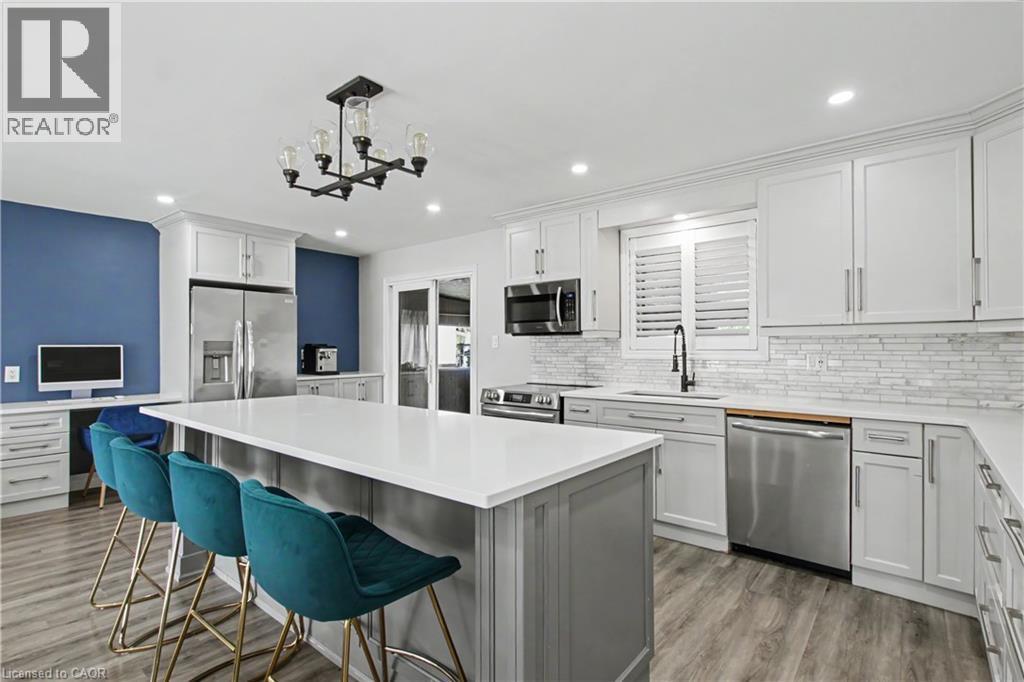 Spacious kitchen featuring an expansive central island with a white countertop, extensive white cabinetry, stainless steel appliances, wood-finish flooring, and a workstation alcove - 44 Oakhurst Crescent, Kitchener, ON - Indoor Photo Showing Kitchen With Upgraded Kitchen