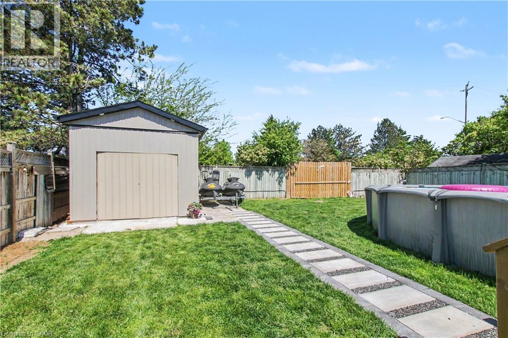 Expansive rear yard featuring a rectangular paver walkway, mature perimeter fencing, and a detached storage shed with a gable roof - 44 Oakhurst Crescent, Kitchener, ON - Outdoor With Backyard