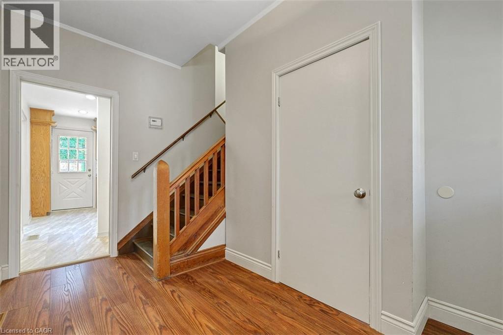 Wood-finish flooring extending into the foreground, a wooden staircase with balusters and handrail, and light gray painted walls - 14 Niagara Street, Hamilton, ON