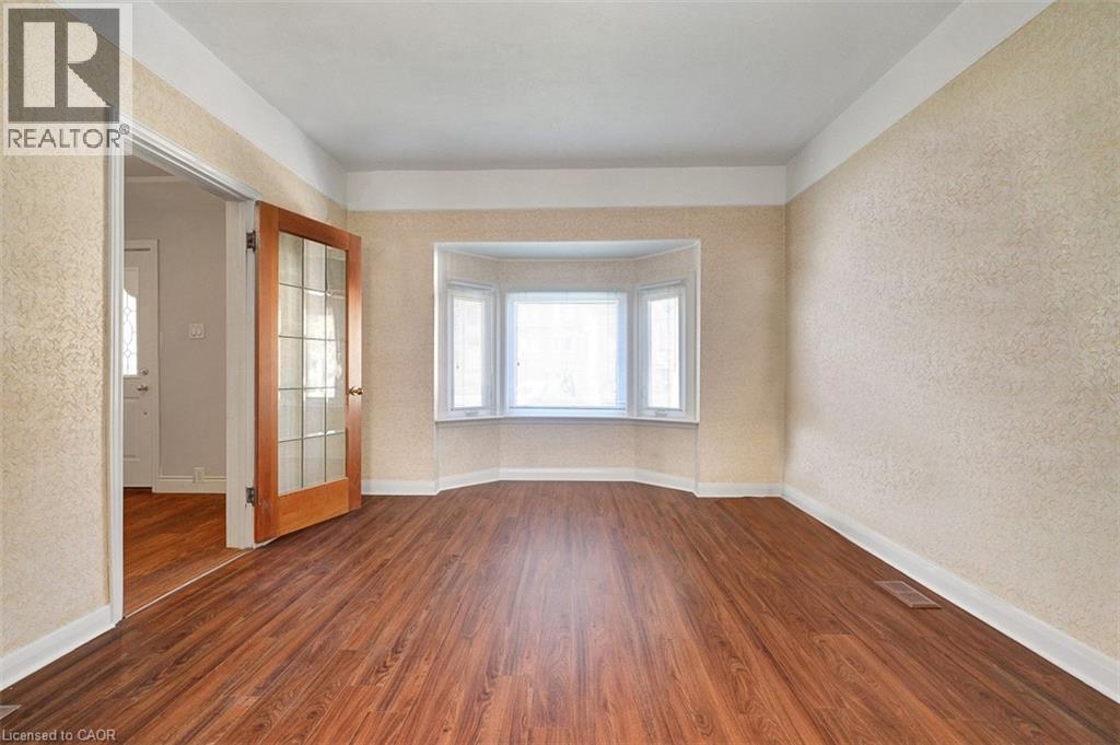 Spacious room featuring wood-finish flooring, a bay window with white trim, and a paneled glass door - 14 Niagara Street, Hamilton, ON