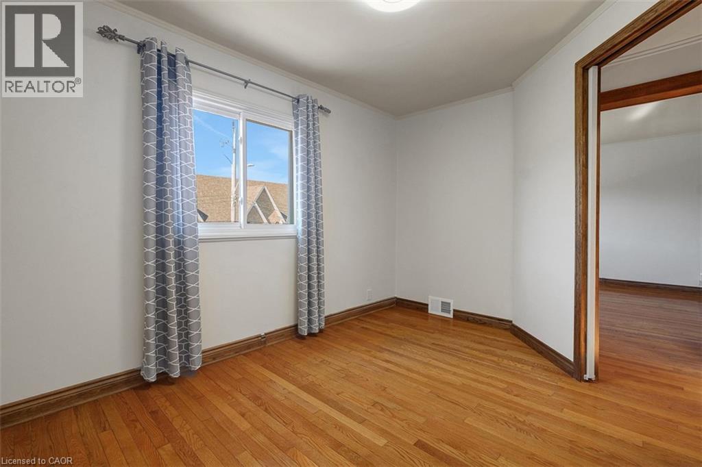 Room featuring wood-finish flooring, white painted walls, a double-hung window, and wood trim - 14 Niagara Street, Hamilton, ON