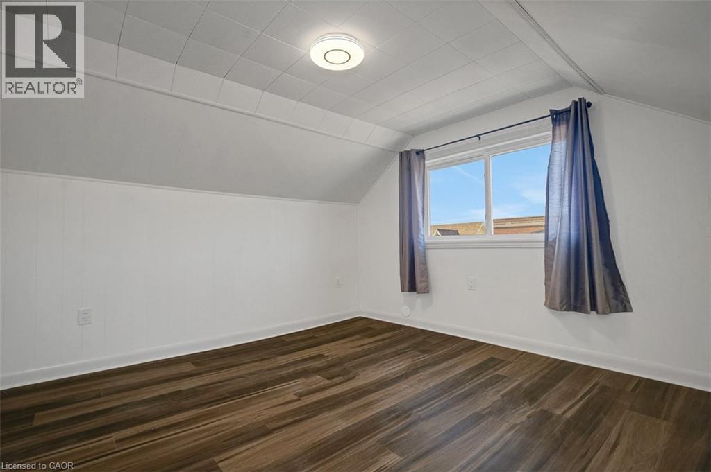 Room featuring wood-finish flooring, white paneled walls, a single window, and a flush-mount ceiling light fixture - 14 Niagara Street, Hamilton, ON