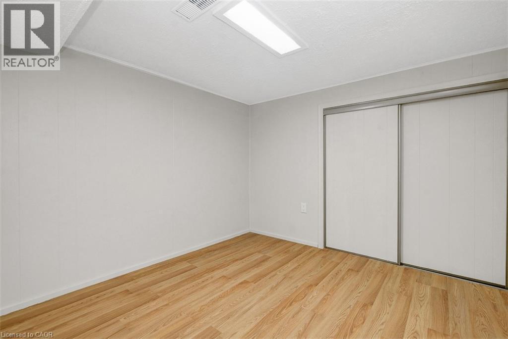 Room featuring wood-finish flooring, light-toned wall paneling, and a dual sliding-door closet with metal frames - 14 Niagara Street, Hamilton, ON
