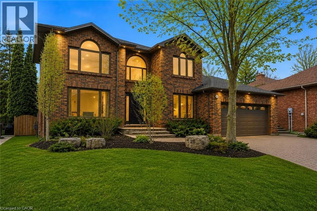 Two-story brick exterior residence featuring a front-facing attached garage, arched window accents, a paved driveway, and mature landscaping - 28 Deerview Avenue, Ancaster, ON