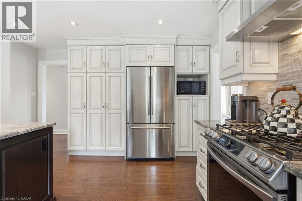 Kitchen featuring stainless steel appliances, light stone countertops, dark wood-style floors, recessed lighting, and backsplash - 28 Deerview Avenue, Ancaster, ON