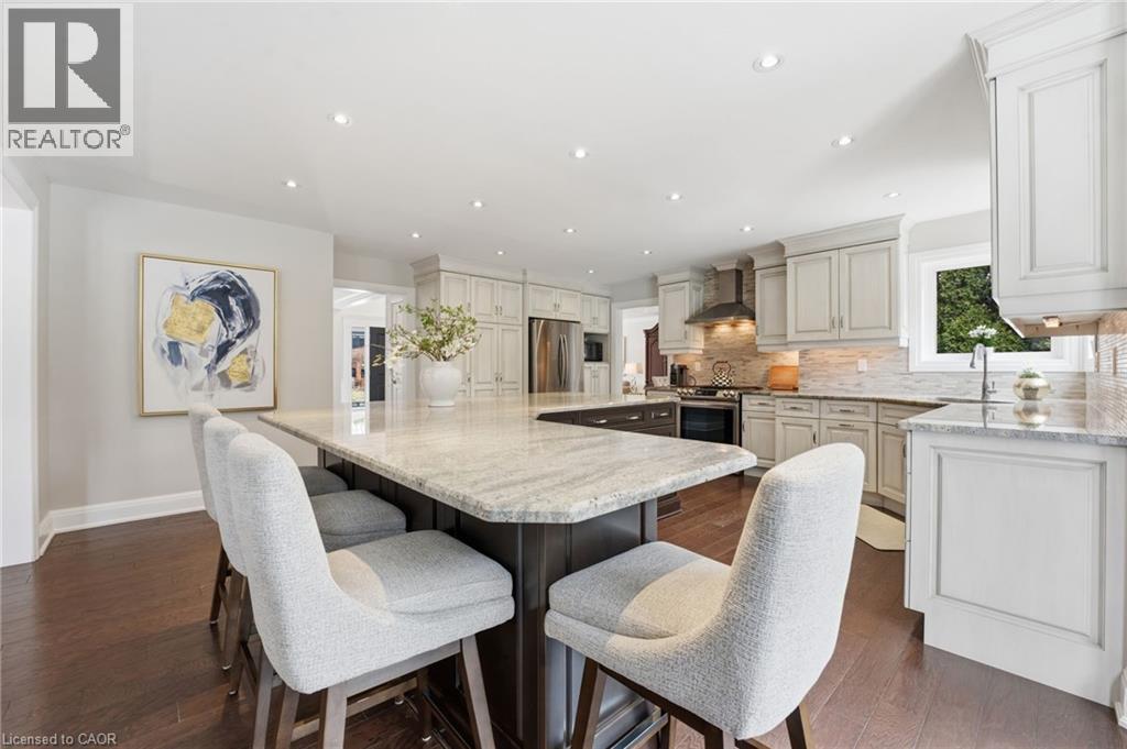 Dual tone kitchen with a large island, light stone countertops, dark wood-style flooring, recessed lighting, and stainless steel appliances - 28 Deerview Avenue, Ancaster, ON