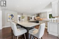 Dual tone kitchen with a large island, light stone countertops, dark wood-style flooring, recessed lighting, and stainless steel appliances -