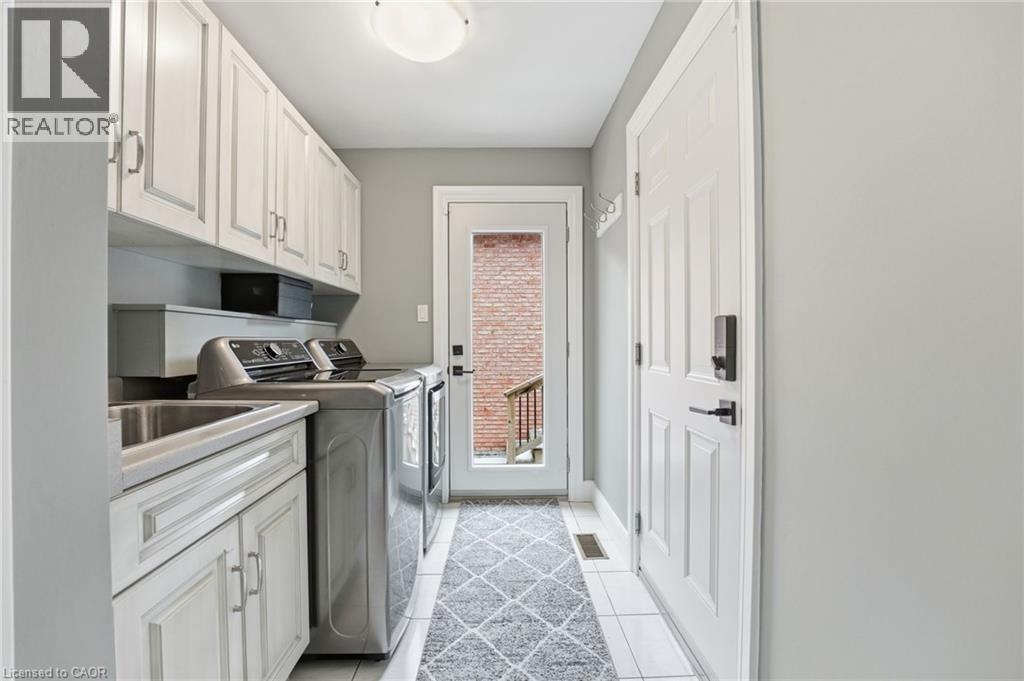 Laundry area with washing machine and dryer, cabinet space, and light tile patterned floors - 28 Deerview Avenue, Ancaster, ON