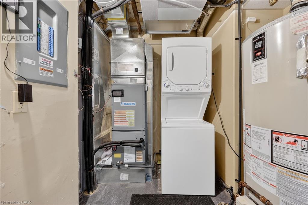 Laundry area with water heater, stacked washer and dryer, electric panel, and heating unit - 90 Highland Drive Unit# 2014/15, Simcoe, ON