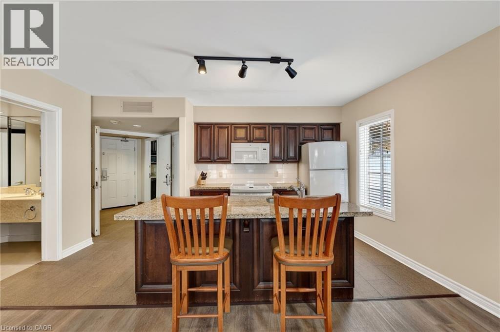 Kitchen featuring dark wood finish cabinets, white appliances, light wood finished floors, a kitchen breakfast bar, and track lighting - 90 Highland Drive Unit# 2014/15, Simcoe, ON