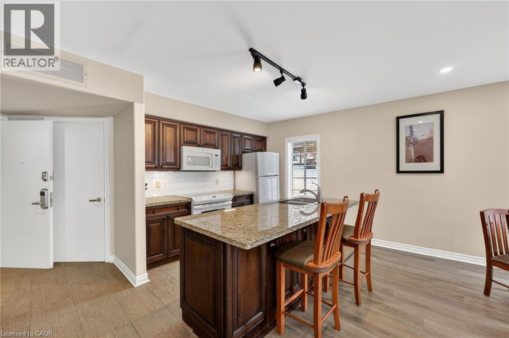 Kitchen with rail lighting, white appliances, backsplash, light stone counters, and a breakfast bar area - 90 Highland Drive Unit# 2014/15, Simcoe, ON