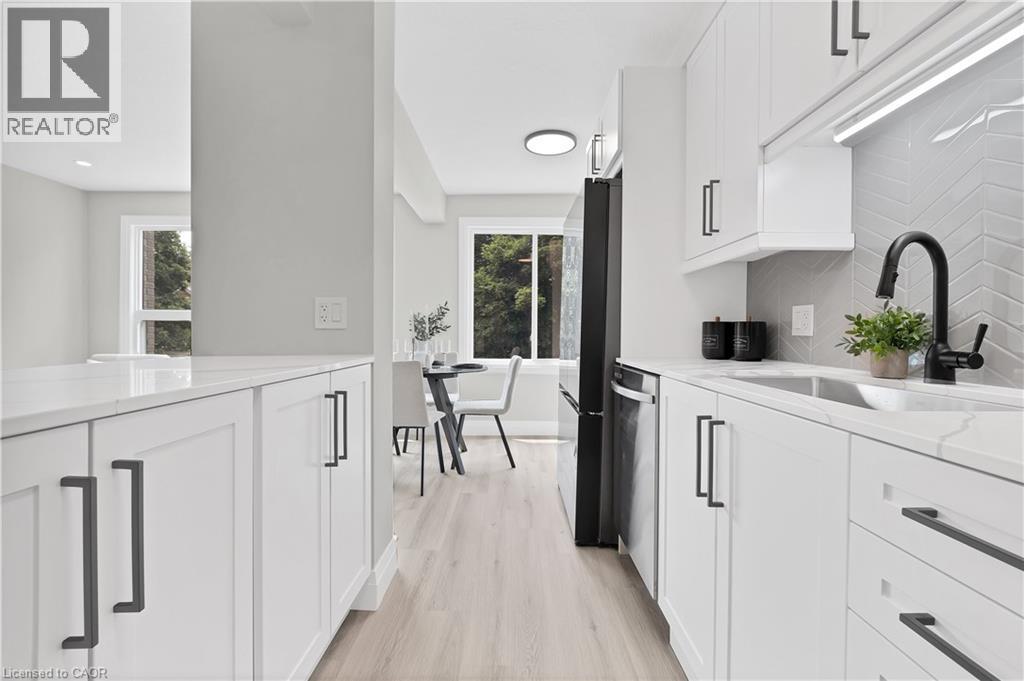 Bright kitchen featuring white shaker cabinetry, quartz countertops, a herringbone tile backsplash, and wood-finish flooring - 71 Blucher Street Unit# G, Kitchener, ON