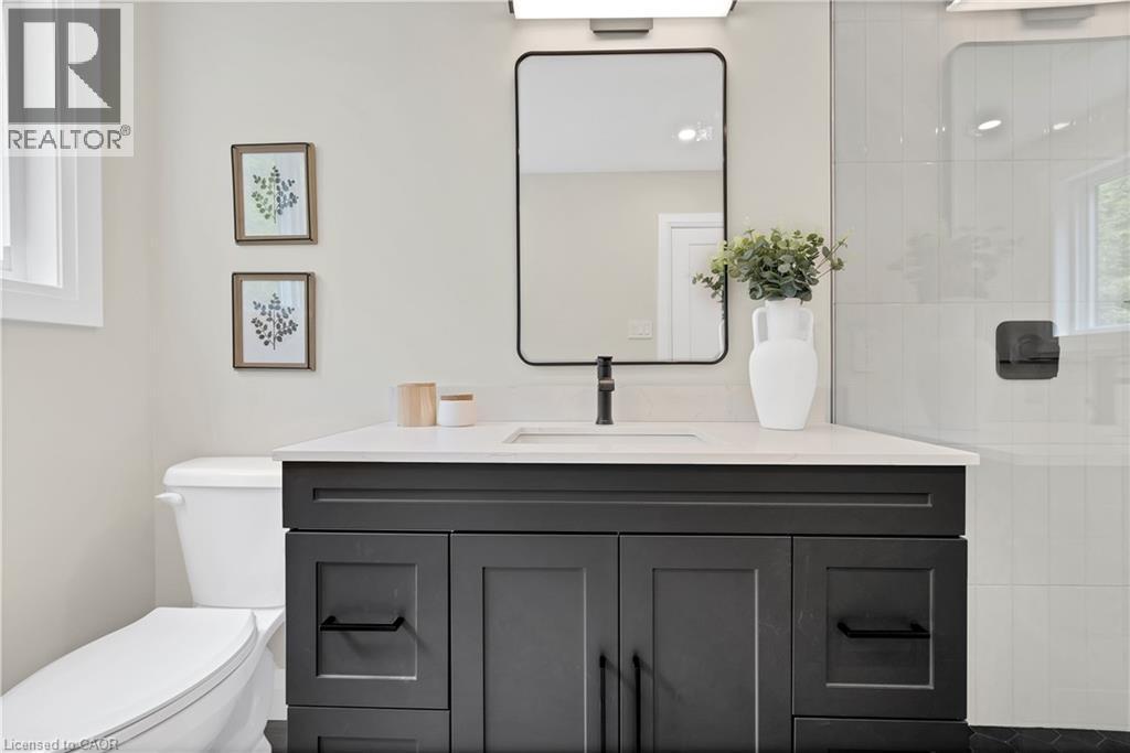 Bathroom featuring a dark wood-finish vanity with a light countertop, a rectangular mirror with a black frame, and a glass-enclosed shower with white tiled walls - 71 Blucher Street Unit# G, Kitchener, ON