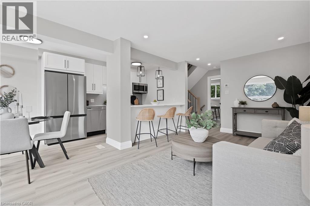Open-concept living area featuring light wood-finish flooring, recessed lighting, a kitchen with stainless steel appliances, white cabinetry, and a breakfast bar - 71 Blucher Street Unit# G, Kitchener, ON