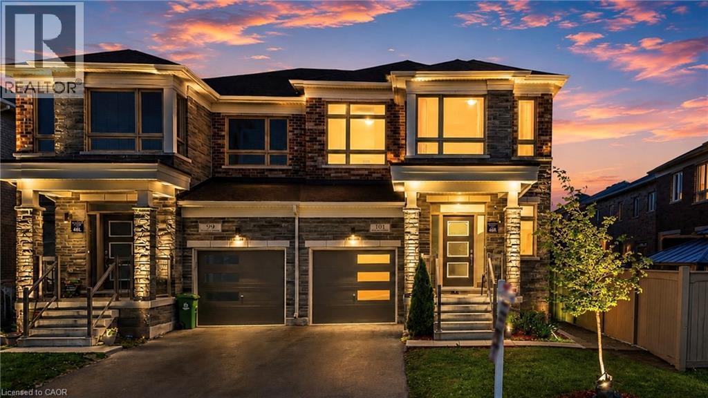 Contemporary semi-detached exterior with a stone and brick facade, multiple large windows, and a black shingle roof. Virtual Twilight - 101 Westfield Crescent, Waterdown, ON