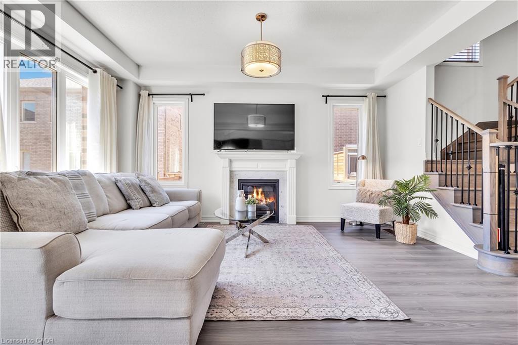 Spacious living area featuring a fireplace with a white mantel, large windows, wood-finish flooring, and a hardwood staircase with black iron spindles - 101 Westfield Crescent, Waterdown, ON