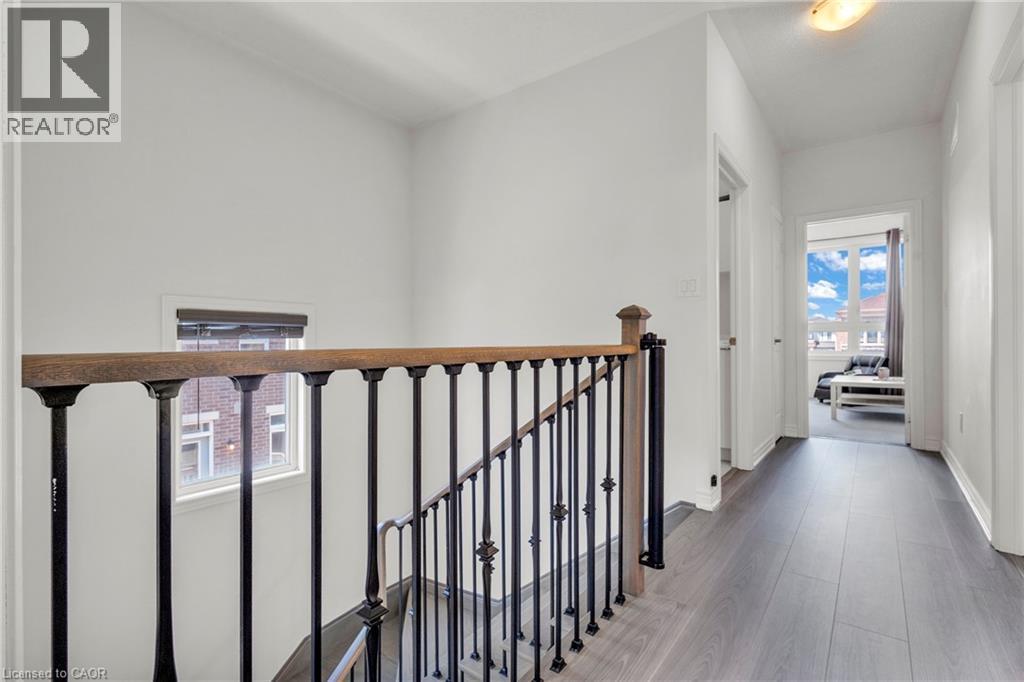 Upper-level hallway featuring wood-finish flooring, white walls, and a staircase with a wood handrail and black metal balusters - 101 Westfield Crescent, Waterdown, ON