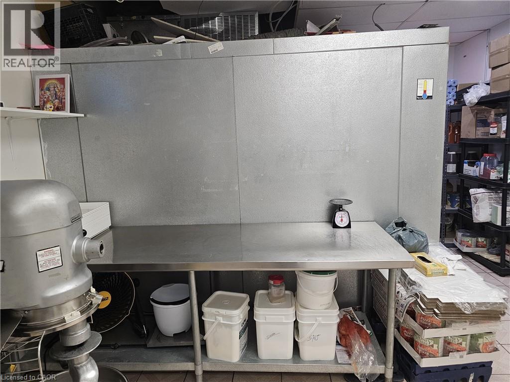 Commercial-grade stainless steel work table with integrated shelving and a large walk-in cooler, featuring additional metal shelving units for storage - 71 Ross Street Unit# 2, St. Thomas, ON