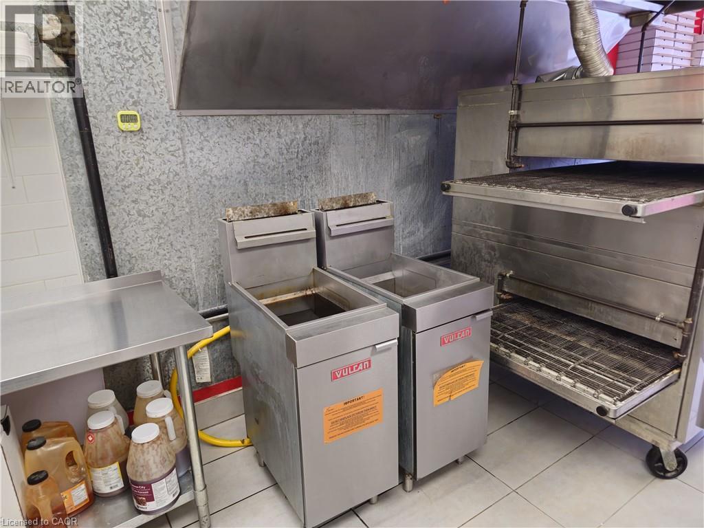 Commercial kitchen featuring stainless steel fryers, a large conveyor oven, and tiled flooring - 71 Ross Street Unit# 2, St. Thomas, ON