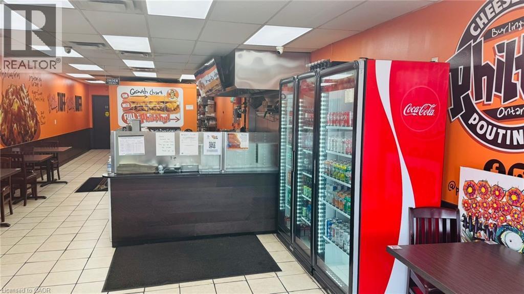 Commercial kitchen space featuring a service counter with a dark wood-finish front, stainless steel overhead exhaust hood, and three glass-front display refrigerators - 2405 Fairview Street, Burlington, ON