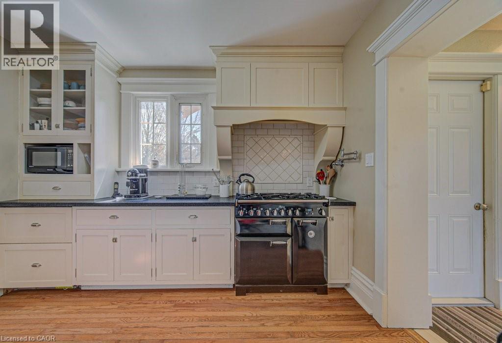 Gourmet kitchen featuring a built-in range, custom cabinetry with glass-front uppers, a built-in microwave, dark countertops, and wood-finish flooring - 2032 Coronation Boulevard, Cambridge, ON - Indoor Photo Showing Other Room