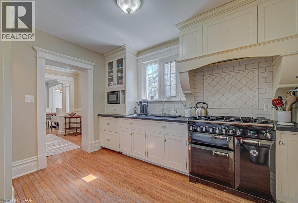 Kitchen featuring wood-finish flooring, white cabinetry, dark countertops, and a subway tile backsplash with a diamond pattern accent - 2032 Coronation Boulevard, Cambridge, ON - Indoor Photo Showing Kitchen