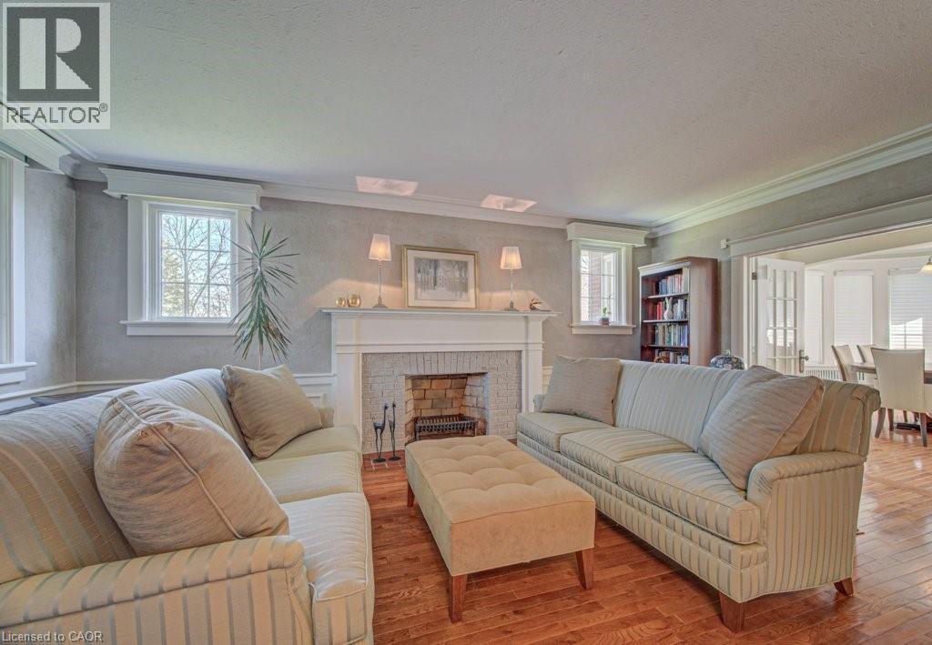 Living area featuring wood-finish flooring, a white mantel fireplace with brick surround, built-in shelving, and white trim - 2032 Coronation Boulevard, Cambridge, ON - Indoor Photo Showing Living Room With Fireplace