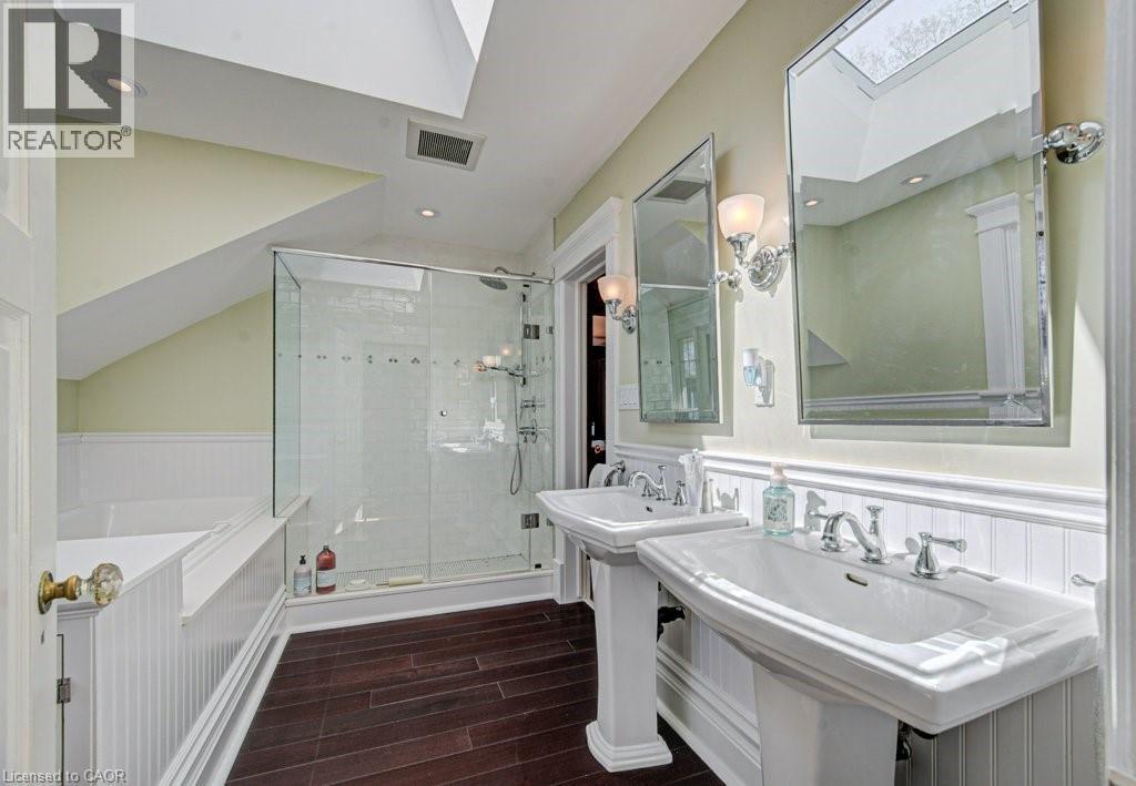 Bathroom featuring wood-finish flooring, dual pedestal sinks, a glass-enclosed shower, a built-in tub, and overhead skylights - 2032 Coronation Boulevard, Cambridge, ON - Indoor Photo Showing Bathroom