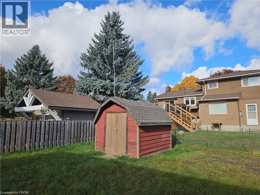 Expansive backyard featuring a red storage shed with a gambrel roof, chain-link fencing, and a wooden privacy fence - 66 Summit Avenue, Kitchener, ON - Outdoor