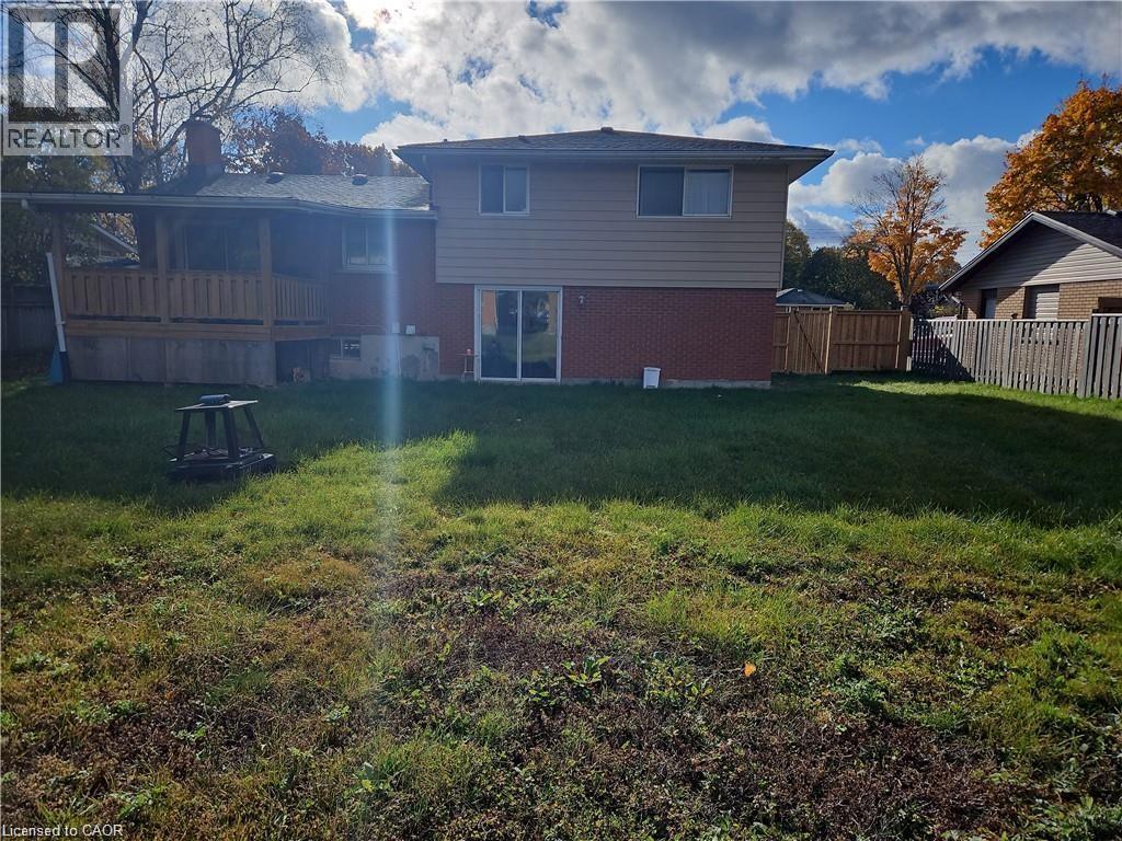 Expansive rear yard featuring a covered wooden deck, brick and siding exterior, sliding glass door, and wooden privacy fence - 66 Summit Avenue, Kitchener, ON - Outdoor