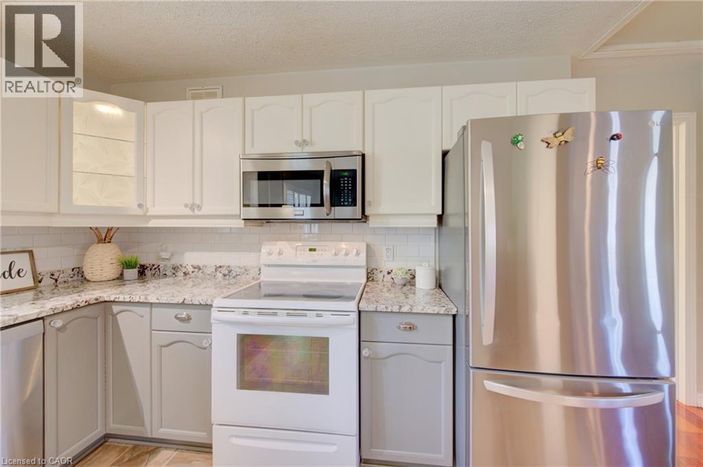Kitchen featuring two-tone cabinetry with upper white cabinets and lower gray cabinets, speckled countertops, a white subway tile backsplash, and stainless steel appliances including an over-the-range - 137 Wesley Crescent, Waterloo, ON