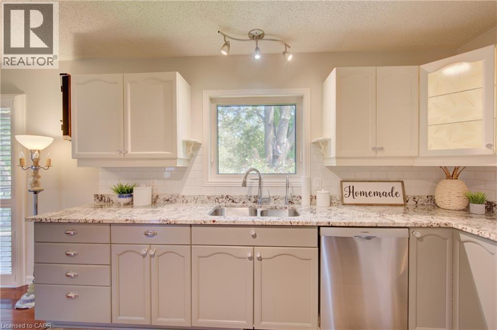 Kitchen featuring white upper cabinetry, grey lower cabinetry, granite countertops, a stainless steel double basin sink with a gooseneck faucet, and a stainless steel dishwasher - 137 Wesley Crescent, Waterloo, ON