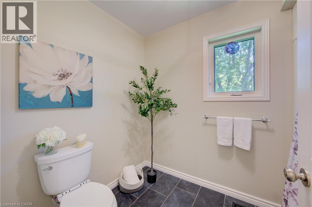 Compact bath with dark tiled flooring, a white toilet, and a single window offering exterior light - 137 Wesley Crescent, Waterloo, ON