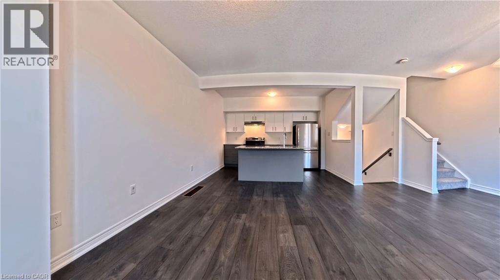 Open-concept living space with dark wood-finish flooring, recessed lighting, and a modern kitchen featuring white upper cabinetry, dark lower cabinetry, and stainless steel appliances - 10 Birmingham Drive Unit# 129, Cambridge, ON - Indoor