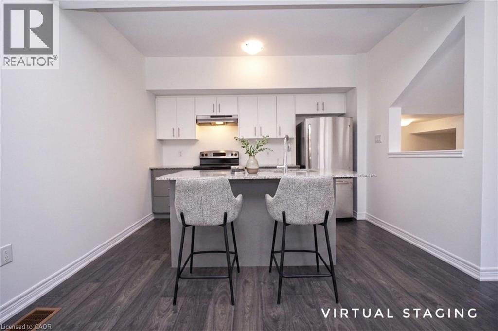 Modern kitchen featuring an island with a light-toned countertop, stainless steel appliances, white cabinetry, and dark wood-finish flooring - 10 Birmingham Drive Unit# 129, Cambridge, ON - Indoor Photo Showing Kitchen With Stainless Steel Kitchen