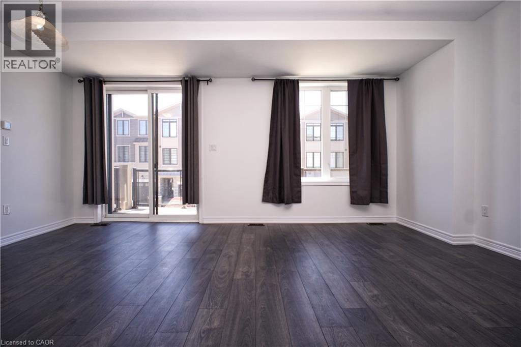 Spacious interior featuring dark wood-finish flooring, white walls, and bright natural light from multiple windows and a sliding glass door - 10 Birmingham Drive Unit# 129, Cambridge, ON - Indoor Photo Showing Other Room