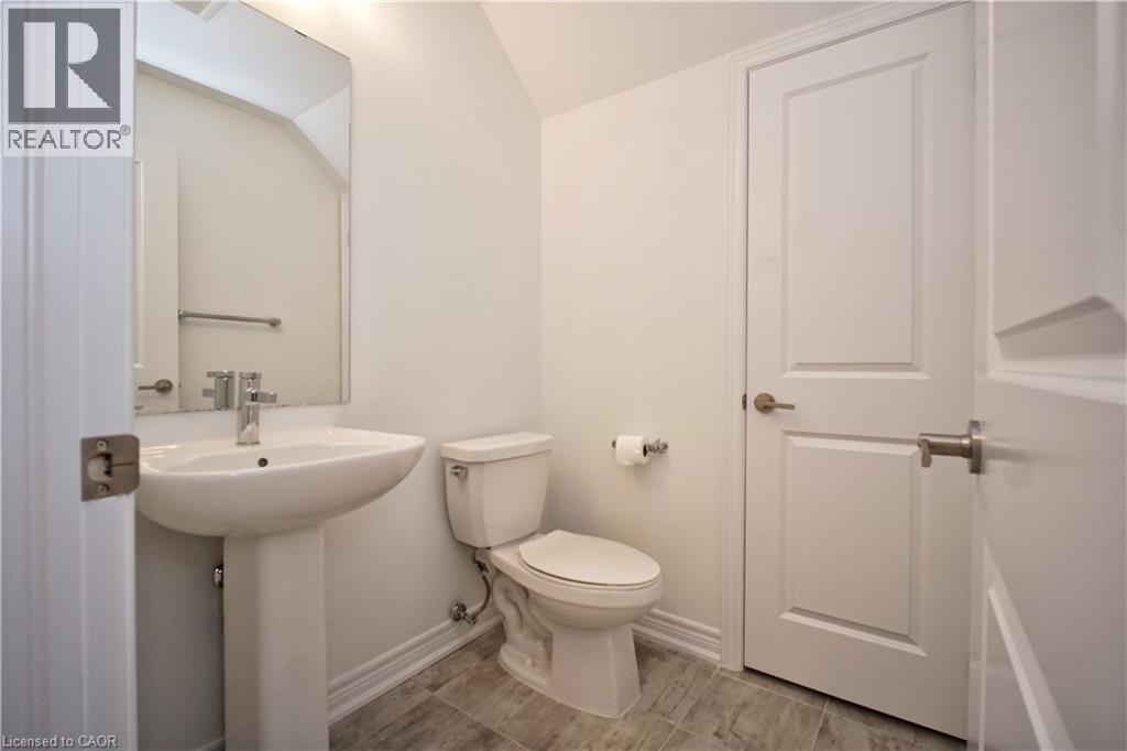 Pedestal sink with chrome faucet, large rectangular mirror, and light gray wood-finish floor tiling - 10 Birmingham Drive Unit# 129, Cambridge, ON - Indoor Photo Showing Bathroom