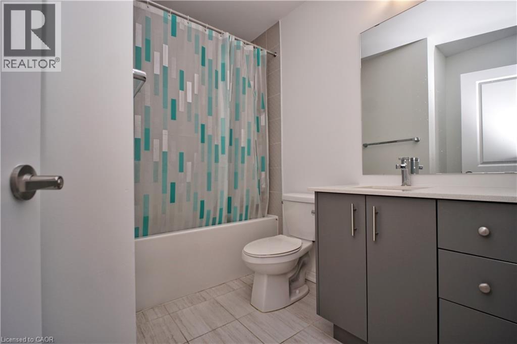 Bathroom featuring a white tub, toilet, and a vanity with gray cabinetry and a light-toned countertop - 10 Birmingham Drive Unit# 129, Cambridge, ON - Indoor Photo Showing Bathroom