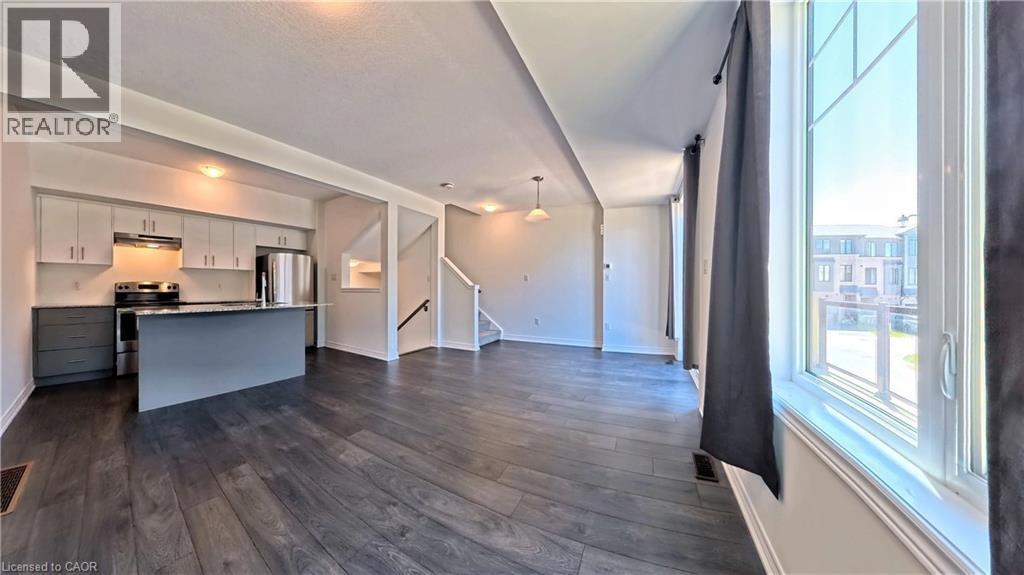 Open-concept living space featuring wood-finish flooring, a modern kitchen island with seating, stainless steel appliances, and a staircase with a dark wood handrail - 10 Birmingham Drive Unit# 129, Cambridge, ON - Indoor Photo Showing Kitchen