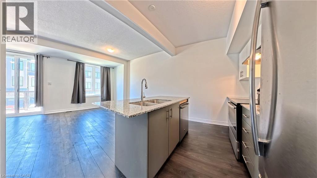 Open-concept living area with dark wood-finish flooring, a kitchen island featuring a double sink and light-colored granite countertop, and stainless steel appliances - 10 Birmingham Drive Unit# 129, Cambridge, ON - Indoor Photo Showing Kitchen With Stainless Steel Kitchen With Double Sink