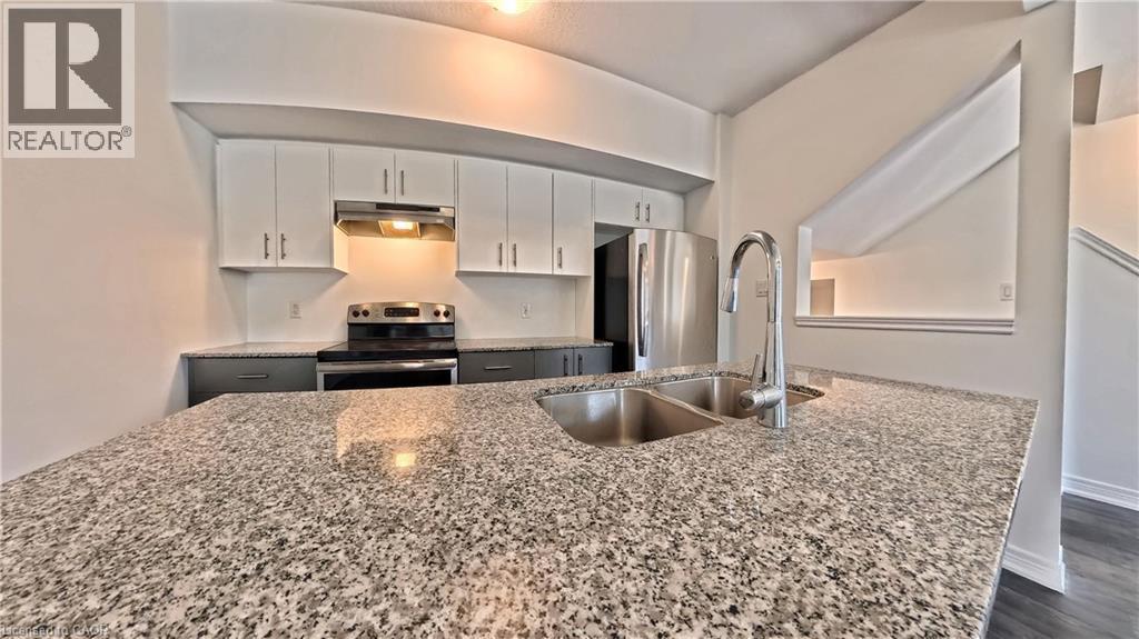 Kitchen featuring a double basin stainless steel sink with a high-arch faucet, granite countertops, stainless steel appliances, and white upper cabinetry with dark lower cabinetry - 10 Birmingham Drive Unit# 129, Cambridge, ON - Indoor Photo Showing Kitchen With Stainless Steel Kitchen With Double Sink With Upgraded Kitchen