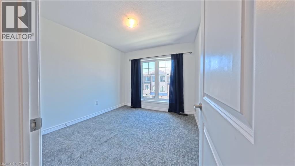 Bright room featuring light gray carpeting, crisp white walls, a large window with dark blue drapes, and a ceiling-mounted light fixture - 10 Birmingham Drive Unit# 129, Cambridge, ON - Indoor Photo Showing Other Room