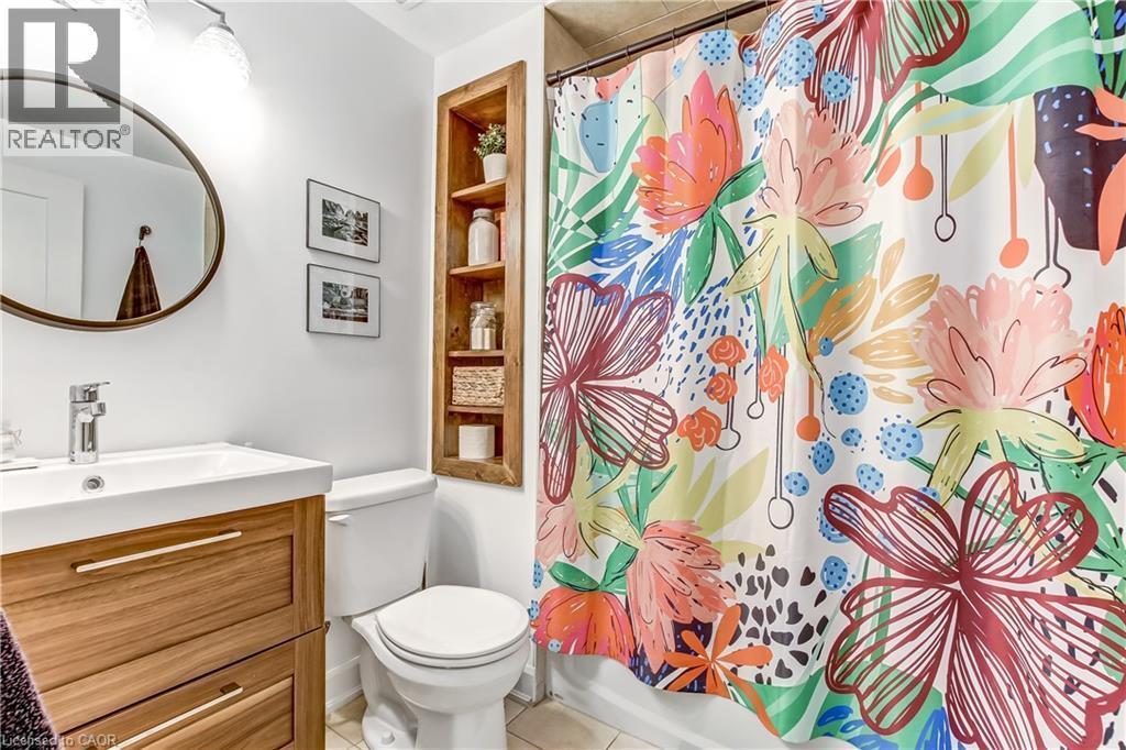 Bathroom featuring a wood-finish vanity with an integrated sink, a circular mirror, and an in-wall wood-finish shelving unit - 218 Richardson Drive Unit# 26, Port Dover, ON