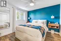 Bedroom featuring a vibrant accent wall, wood-finish flooring, a built-in ceiling fan, and a double-pane window -