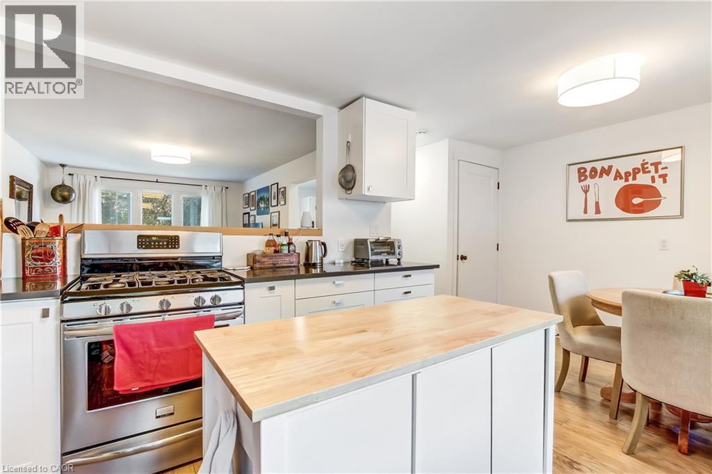 Kitchen featuring an island with a wood-finish countertop, stainless steel gas range, white cabinetry, dark countertops, and wood-finish flooring - 218 Richardson Drive Unit# 26, Port Dover, ON