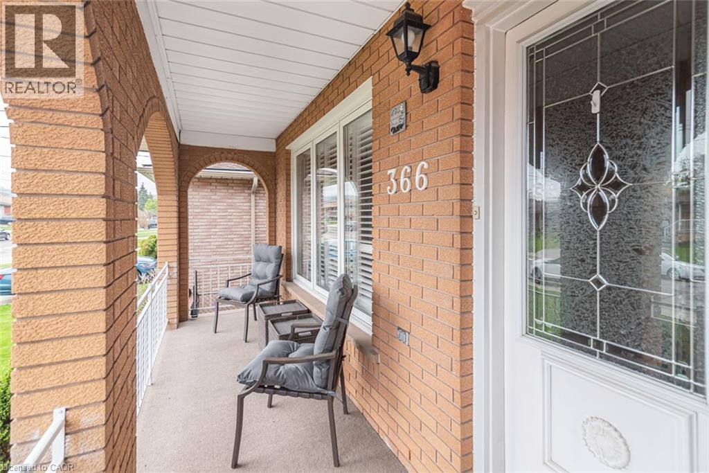 Covered front porch featuring arched brickwork, a decorative glass entry door, white window blinds, an exterior wall sconce, and a white metal railing - 366 Berkindale Drive, Hamilton, ON