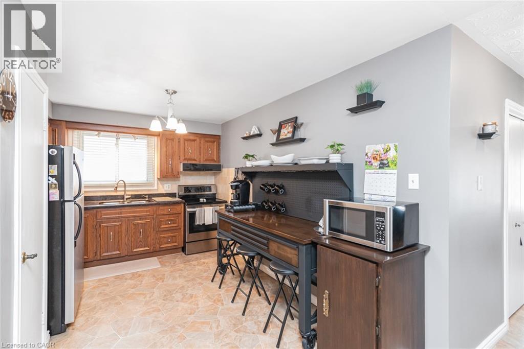 Kitchen featuring wood cabinetry, stainless steel appliances, a window with horizontal blinds, a single-basin sink with a gooseneck faucet, and light-toned tile flooring - 366 Berkindale Drive, Hamilton, ON