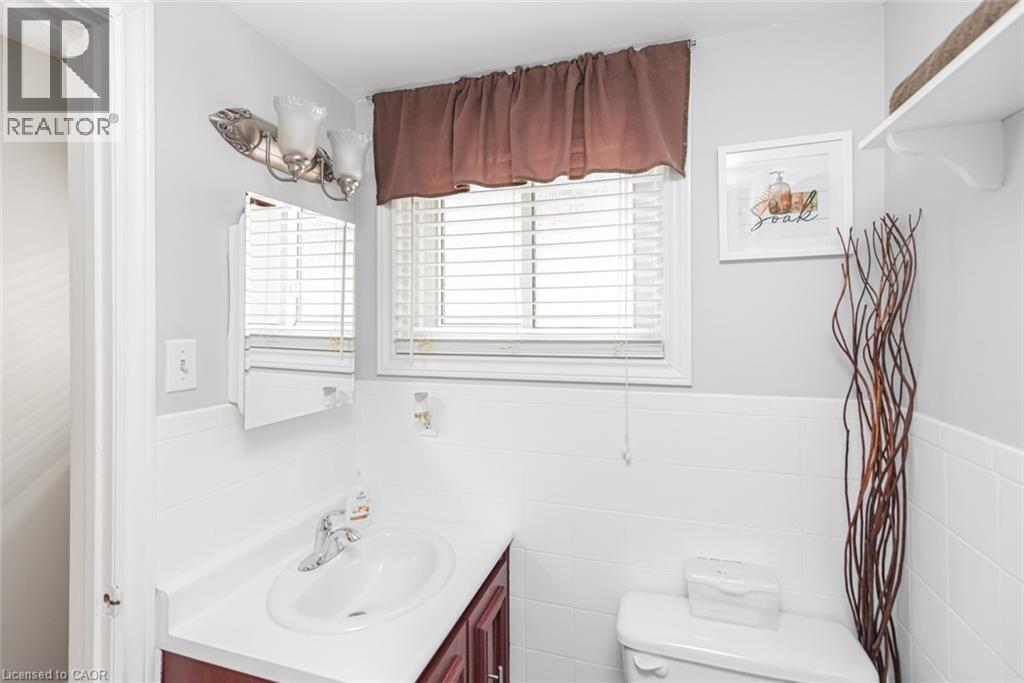 Bathroom featuring a window with blinds, a vanity with an integrated sink, a wall-mounted medicine cabinet, and a two-bulb light fixture - 366 Berkindale Drive, Hamilton, ON