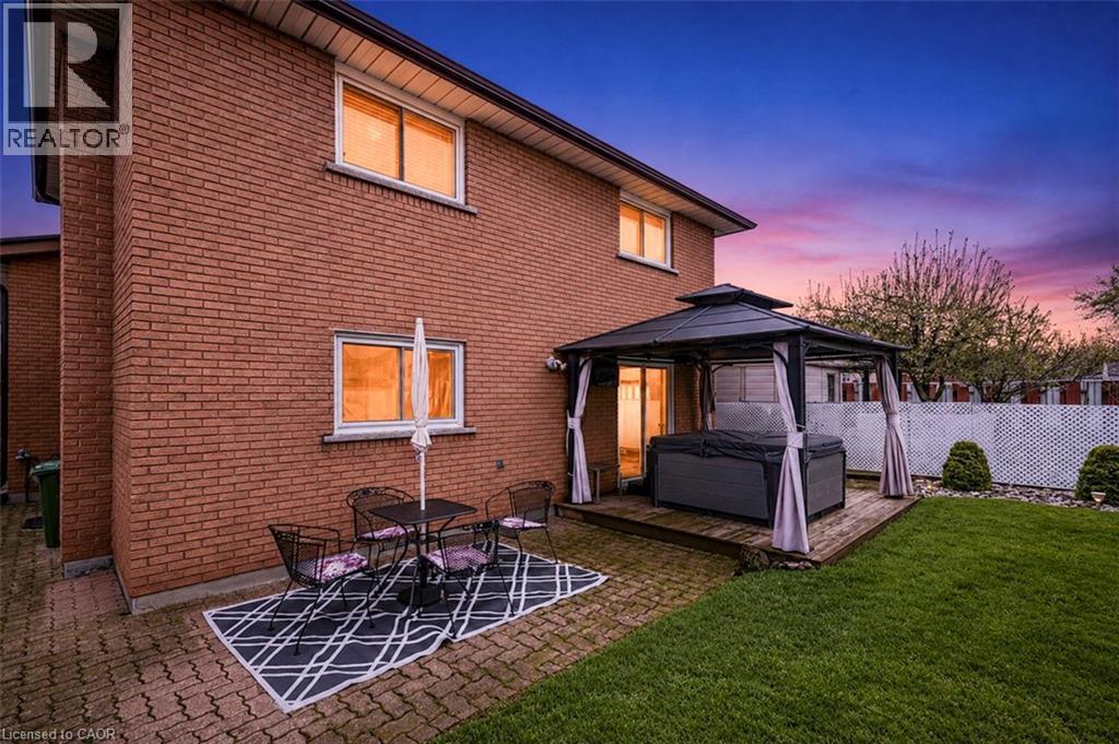 Rear exterior featuring brick facade, a paver patio, green lawn, and a fenced perimeter - 366 Berkindale Drive, Hamilton, ON
